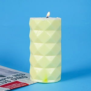 Detail shot of a cream-colored geometric diamond pattern pillar candle lit against blue background