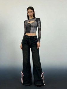 Dettaglio di jeans neri a vita alta e gamba larga con decorazioni a fiocco rosa laterali
