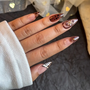 Brown almond press-on nails with 3D floral accents and zebra patterns on hands