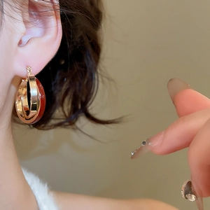 Close-up of model wearing gold criss-cross hoop earrings with red oil-dripped finish
