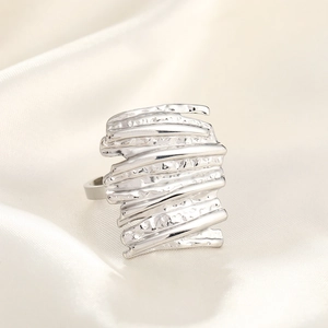 Close-up of a silver hammered texture wide ring on cream silk fabric background