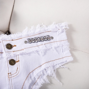 Dettaglio di pantaloncini in denim bianco con strass scintillanti e borchie in metallo argento