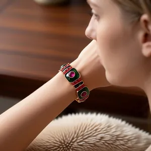 Bracciale vintage placcato oro con smalto verde e pietre rosse su un polso femminile