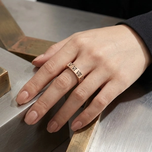 Dettaglio anello oro rosa con numeri romani su dito di modella e sfondo in marmo