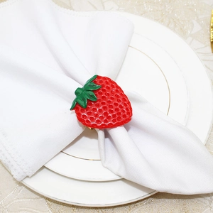 Detail of a bright red strawberry napkin ring on a white plate with gold rim