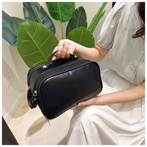 Detail of hand-held black PU leather makeup bag with dual zipper and gold hardware