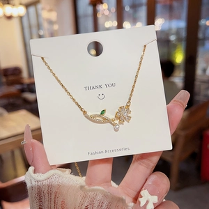Close-up of a gold leaf necklace with green stones and a white pearl on a display card