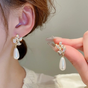 Detail of gold-plated leaf earring with sparkling rhinestones and drop pearl pendant