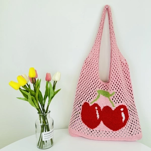 Detail of pink knitted mesh tote bag featuring red cherry pattern and hollow-out texture
