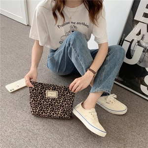 Leopard print canvas bag with gold logo tag held by hand in a casual outdoor setting