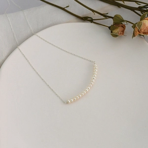 Detailed shot of a minimalist silver pearl necklace arranged on a white ceramic plate