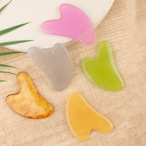 Set of five heart-shaped resin facial massage tools in various marble finishes on a wooden surface