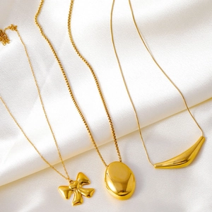 Colliers minimalistes en acier doré avec pendentifs nœud et ovale sur fond de soie