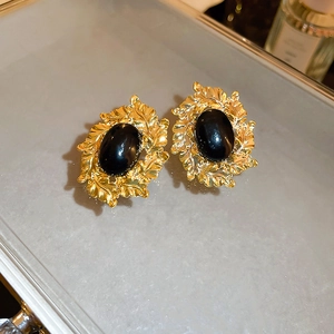 Macro view of vintage gold leaf earrings with a large black oval gemstone centerpiece