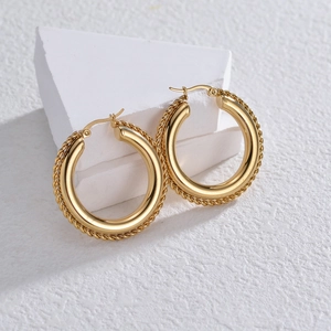 Detailed close-up of golden hoop earrings with twisted rope texture on white stone