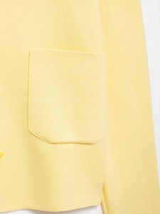 Detail of light yellow knit cardigan featuring a rounded patch pocket and button texture