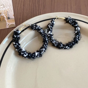 Gros plan sur les boucles d'oreilles créoles dorées enveloppées de fil tricoté noir et blanc