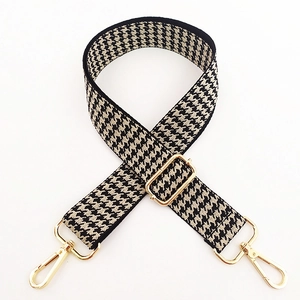 Detail of adjustable houndstooth bag strap with golden buckles and lobster clasps