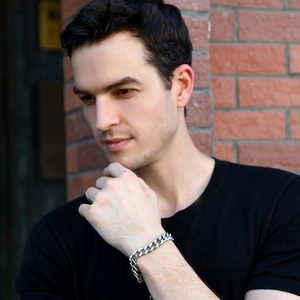 Close-up of a silver Cuban link bracelet on a male wrist against a brick wall background