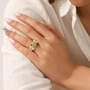 Detail of bohemian gold ring with white pearls and green stones on model's finger