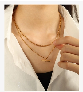 Détail d'un collier double rang doré avec fermoir OT porté sur une chemise blanche