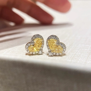 Belles boucles d'oreilles cœur dorées avec zircons jaunes et blancs sur surface douce
