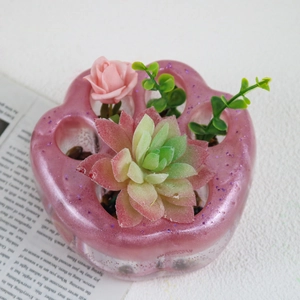 Detalle de maceta de resina garra de gato rosa con purpurina y plantas artificiales