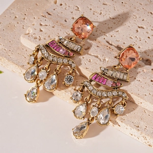 Detailed shot of vintage gold drop earrings with pink gems and crystals on beige stone