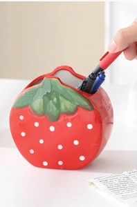 Close-up of hand placing a pen into a red ceramic strawberry pencil holder for desk