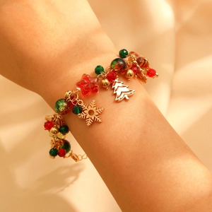 Detailed view of Christmas charm bracelet with gold snowflake, tree and red beads
