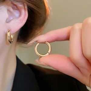 Minimalist gold hoop earrings with polished finish shown on ear and held by hand