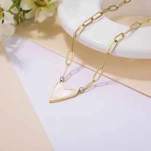 Detailed shot of golden chain necklace featuring a heart-shaped white shell pendant