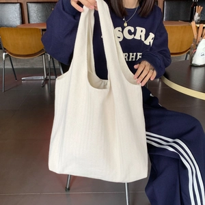 Detail of off-white tote bag with herringbone texture carried by model in a cafe setting