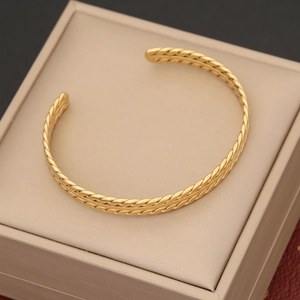 Detail of a golden twisted rope bangle placed on a beige jewelry box with metallic finish
