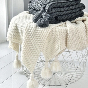 Close-up of waffle knit throw blankets with tassels in a minimalist wire basket