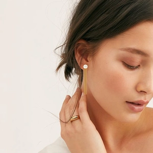 Elegant pearl tassel earrings with gold chains and minimalist gold band ring on model