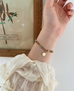 Detail of gold-plated thick chain bracelet with colorful enamel dots and Lucky coin charm