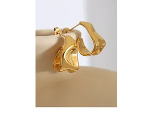 Vue détaillée de boucles d'oreilles dorées irrégulières en forme de C sur céramique avec finition polie