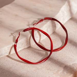 Macro view of red twisted geometric hoop earrings with textured lacquer finish