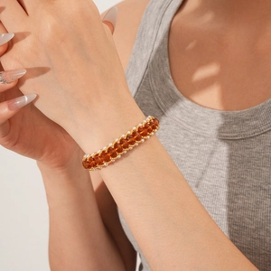 Detail of woven pearl and amber crystal bracelet with gold clasp on a model's wrist