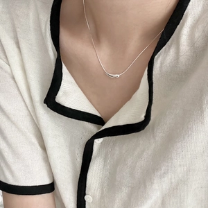Close-up of a minimalist silver teardrop pendant necklace worn over a white knit sweater