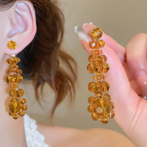Close-up of elegant amber crystal flower tassel earrings worn with a chic hand pose