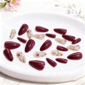 Long almond press-on nails with burgundy finish and delicate floral designs on a white tray