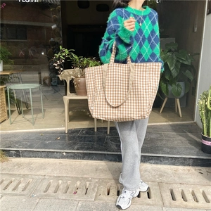 Close-up of brown and white checkered canvas tote bag worn by a model in casual street style