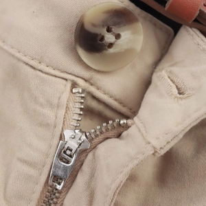 Detailed macro view of the solid beige casual shorts featuring a metal zipper and button