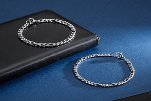 Macro detail of two silver Figaro chain bracelets in stainless steel on a dark surface