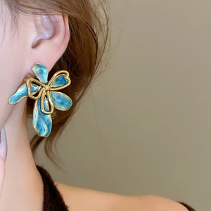 Primo piano di orecchini a fiore in smalto blu con bordo dorato indossati da una modella