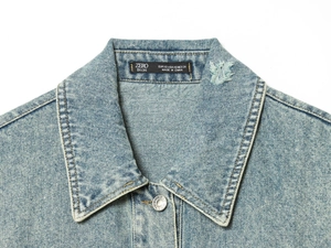 Detailed close-up of light blue denim jacket collar with metallic buttons and size label
