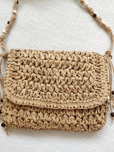 Handmade woven straw crossbody bag with wood bead strap and flap closure for beach vacations
