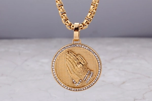 Macro shot of 18K gold plated prayer hands round pendant with sparkling crystals